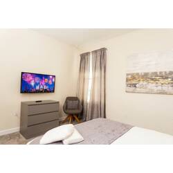 Rest in a bright and cozy bedroom with a comfortable bed, soft white bedding, gray accents, elegant headboard, bedside lamps, neutral curtains, carpeted floor, and warm decor.