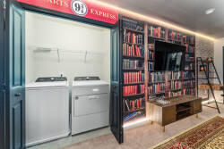 This stylish nook offers a sleek washer and dryer behind charming double doors, with a captivating wall of books inviting you to unwind. The warm lighting and rich textures create a cozy atmosphere, ideal for relaxation.