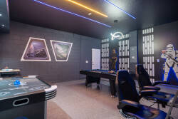 Enter a lively game room with sleek gaming chairs and vibrant neon lights that bring a futuristic touch. Enjoy custom space-themed wall art that enhances the immersive atmosphere for your entertainment and relaxation.