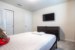 This cozy bedroom invites you to relax with a plush bed dressed in fresh linens and soft towels. The warm wood furnishings and soft, neutral walls create a soothing atmosphere, while a sleek flat-screen TV adds a modern touch.