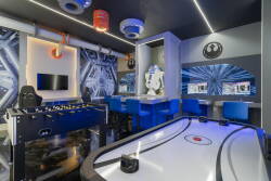 Welcome to our vibrant game room, where a sleek foosball table and air hockey setup await you. The bold blue accents and stylish lighting create an energetic atmosphere, inviting fun and competition for guests of all ages.