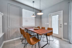 Join us at the stylish wood dining table, surrounded by sleek tan chairs against soft gray walls. Enjoy warm natural light flooding in, creating the perfect atmosphere for shared meals and casual conversations.