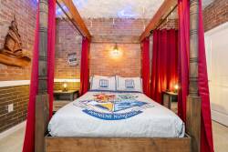 Immerse yourself in a cozy atmosphere featuring exposed brick and warm pendant lights above a rustic four-poster bed. Rich red drapes frame the comfy bedding with unique designs, making it a perfect retreat for relaxation.