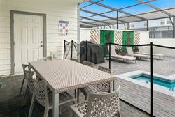 Enjoy a covered patio with outdoor dining, grill, screened pool area, lounge chairs, and a safety fence, creating a comfortable space for family meals and relaxing vacation moments.