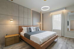 This cozy bedroom, filled with natural light, offers a stylish wooden bed with plush bedding and modern pillows, along with a sleek nightstand, all in warm tones that create a restful atmosphere for your relaxation.