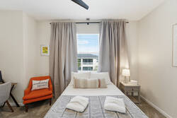 Rest in a cozy bedroom with soft bedding, gray curtains, a bright window, orange accent chair, small desk, bedside lamp, carpeted floor, and warm neutral decor.