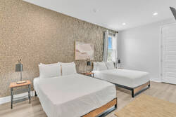 Rest in a bright bedroom with two comfortable beds, soft white bedding, a stylish patterned accent wall, bedside lamps, wood flooring, and neutral decor for a relaxing stay.