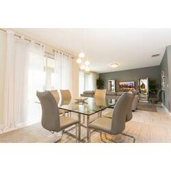 Gather in a bright dining area with a glass table, elegant chairs, pendant lights, soft white curtains, neutral decor, and an open view toward the stylish living room.