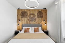 Rest in a cozy Mickey inspired bedroom with a white bed, neutral blanket, wood accent wall, pendant lights, modern ceiling fixture, and soft curtains, creating a warm space for vacation.