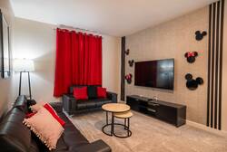Relax in a cozy Mickey themed living room with black leather sofas, red curtains, wall-mounted TV, playful character decor, soft lighting, and nesting coffee tables, creating a fun space for family vacation moments.