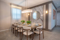 Enjoy delightful meals in this chic dining area, featuring a beautiful chandelier above a spacious table with modern light-colored chairs, accented by an elegant marble wall and fresh greenery for a vibrant and sophisticated.