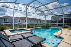 Relax in a private screened pool area with sparkling water, a raised spa, sleek lounge chairs, and open sky views, creating a refreshing space for family vacation moments.
