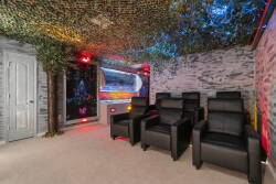 Step into this unique movie room featuring plush black recliners and vibrant, multi-colored lighting that creates an immersive ambiance. The artistic wall design and camo ceiling add a playful touch, perfect for movie nights.