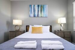 Unwind in this beautifully designed bedroom with a plush bed dressed in crisp linens and cozy pillows. The soft gray walls and vibrant artwork create a warm atmosphere, enhanced by stylish lamps for inviting evenings.