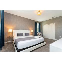 Rest in a stylish bedroom with a comfortable bed, white bedding, gray accents, blue curtains, bedside lamps, textured accent wall, soft carpet, and warm modern decor.