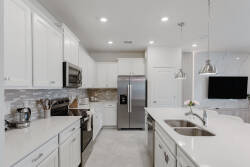 This bright kitchen features sleek white cabinetry and beautiful quartz countertops, creating a polished space for your cooking. Modern stainless-steel appliances and soft pendant lighting add to the warm, inviting atmosphere.