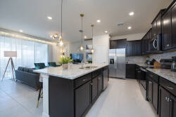 Step into a stylish kitchen featuring rich dark cabinetry and gleaming granite countertops, illuminated by elegant pendant lights. The open layout seamlessly connects to a cozy seating area, perfect for gatherings after meals.