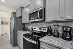 Experience culinary adventures in this well-equipped kitchen featuring sleek gray cabinetry, sparkling granite countertops, and modern appliances, all highlighted by a stylish mosaic backsplash for memorable meals.