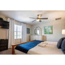 Relax in a bright and airy bedroom with a cozy queen bed adorned in plush blue accents and soft linens. Enjoy the natural light and a stylish dresser with a large mirror, combining charm and functionality for your stay.