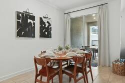 Enjoy a bright and inviting dining area with a charming wooden table, warm natural tones, and modern black-and-white wall decor, all illuminated by large windows that let in abundant sunlight for a delightful dining experience.