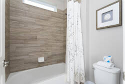 Experience a refreshing bathroom with warm wood-tone tiles and a soothing light-colored shower curtain. Framed artwork adds personality, creating a cozy atmosphere for your daily routines.