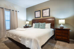 Experience a cozy retreat in this beautifully designed bedroom, featuring a plush king-sized bed with soft linens and decorative pillows. Warm wall tones and rich wood furniture create an inviting ambiance bathed in natural light.