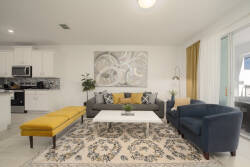 Welcome to a bright living area featuring a cozy gray sofa and a cheerful yellow bench, ideal for relaxation. The artistic wall decor and soft patterned rug enhance the modern kitchen, creating a stylish and inviting atmosphere.