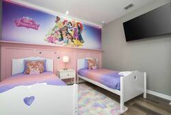 This cheerful bedroom boasts two twin beds with vibrant purple and pastel bedding, a whimsical princess mural to inspire imagination, a cozy nightstand with a soft lamp, and a plush rug that adds warmth and comfort.