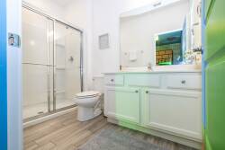 Experience a bright, airy bathroom with sleek glass shower doors and a spacious vanity accented by elegant hardware. The warm wood-like flooring pairs beautifully with fresh white cabinetry, offering a clean and inviting space.