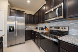 Discover a stylish kitchen with dark cabinetry and stainless steel appliances, ideal for cooking and socializing. Enjoy ample space on elegant granite countertops, complemented by a sophisticated tile backsplash for added charm.