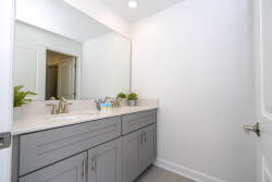 This modern bathroom features sleek gray cabinetry paired with a pristine white countertop, offering a clean and stylish atmosphere. Abundant natural light enhances the spacious feel, while potted greenery adds a refreshing touch.