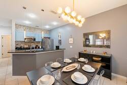 Experience our chic dining area featuring a sleek black table for six, a sparkling mirror, and a contemporary light fixture. The blue-gray walls set a refreshing tone, creating a warm and inviting space for your gatherings.