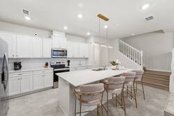 Cook and gather in a bright modern kitchen with white cabinets, stainless steel appliances, a spacious island, soft pendant lighting, plush bar chairs, and playful Mickey decor, perfect for family meals during vacation.