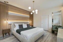 Experience a cozy bedroom with a plush king-sized bed in crisp white linens and a soft dark green throw. The warm wood accents and modern pendant lighting enhance the soothing ambiance, creating a stylish and inviting retreat.