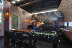Step into a playful escape, featuring a foosball table and a striking mural of a vintage train, perfect for lively evenings with friends. The exposed brick walls and industrial lighting create a unique blend of comfort and style.