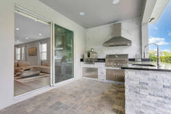 Enjoy a covered outdoor kitchen area with a built-in grill, sink, stone counters, and sliding glass doors leading inside. A comfortable space for cooking, dining, and relaxing by the pool.