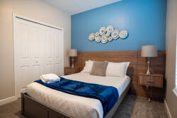 This cozy bedroom features a striking blue accent wall that contrasts perfectly with the warm wooden headboard and nightstands. Plush bedding and inviting pillows create soft textures, while stylish lamps add a touch of elegance.