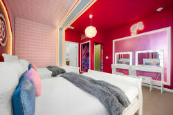 Embrace the playful vibe of this colorful bedroom with bright pink walls, soft bedding, and cozy throw blankets. The chic vanity area with stylish mirrors invites you to relax and refresh after a day of fun adventures.