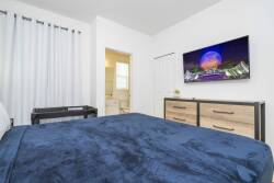 Step into a cozy bedroom that features a plush navy-blue bedspread inviting you to unwind. The sleek dresser complements the crisp white walls, while a large window draped in light curtains fills the space with natural light.