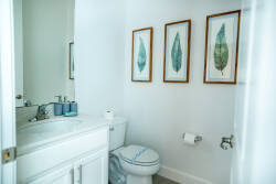 Step into a bright bathroom featuring a pristine white vanity and soothing greenery art adorning the walls. The clean lines and soft color palette create an atmosphere of fresh tranquility, perfect for your daily rituals.
