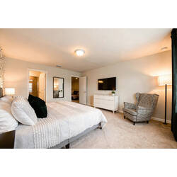 Rest in a spacious bedroom with a white textured bed, green accent pillows, geometric wall, black nightstands, soft lamps, dark curtains, and private bathroom access for vacation comfort.