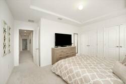 Bright and airy, this bedroom features a plush, neutral-toned bedspread that complements the soft, inviting carpet. The sleek dresser and modern TV provide a cozy atmosphere, while the subtle wall art adds a touch of style.