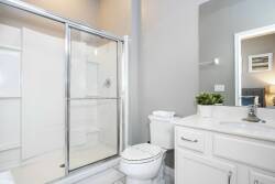 Enjoy a bright bathroom with clean lines and modern fixtures, including a spacious glass shower and a sleek vanity with a fresh plant, all set in neutral tones that enhance the abundant natural light for a refreshing experience.