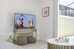 This cozy living area boasts a gold-accented console under a wall-mounted TV, ideal for unwinding with your favorite shows. The soft beige tones and textured poufs create an inviting atmosphere, perfect for relaxation.
