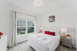 This bright bedroom showcases a plush white bed with striking red accents, creating a vibrant focal point. Large windows invite natural light, and elegant side tables enhance the sophisticated atmosphere for your stay.