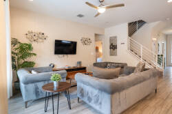 Enter a bright living area with soft gray sofas that beckon you to relax. Natural wood accents and a sleek TV set a cozy yet stylish atmosphere, ideal for unwinding after a day of exploration, complemented by refreshing greenery.
