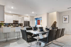 Welcome to a chic dining space featuring a sleek black dining set, softened by recessed lighting. Modern white cabinetry suggests culinary delights, and vibrant artwork brings a bright touch to the atmosphere.