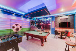 Welcome to our vibrant game room, featuring a classic pool table for friendly competition, a sleek foosball table, and cozy seating, all under dynamic LED lighting—perfect for unforgettable evenings with family and friends.