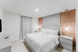 Enjoy restful nights in this inviting bedroom with a plush king-sized bed and crisp white linens. Warm wood paneling and soft lighting create a cozy atmosphere, complemented by stylish nightstands for a modern flair.