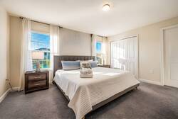 This cozy bedroom, filled with natural light, boasts a plush gray carpet and crisp white linens for restful nights. Its minimalist decor and soft accents create a tranquil atmosphere perfect for relaxation.